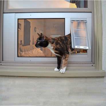 A calico cat is exiting a window through a pet door.