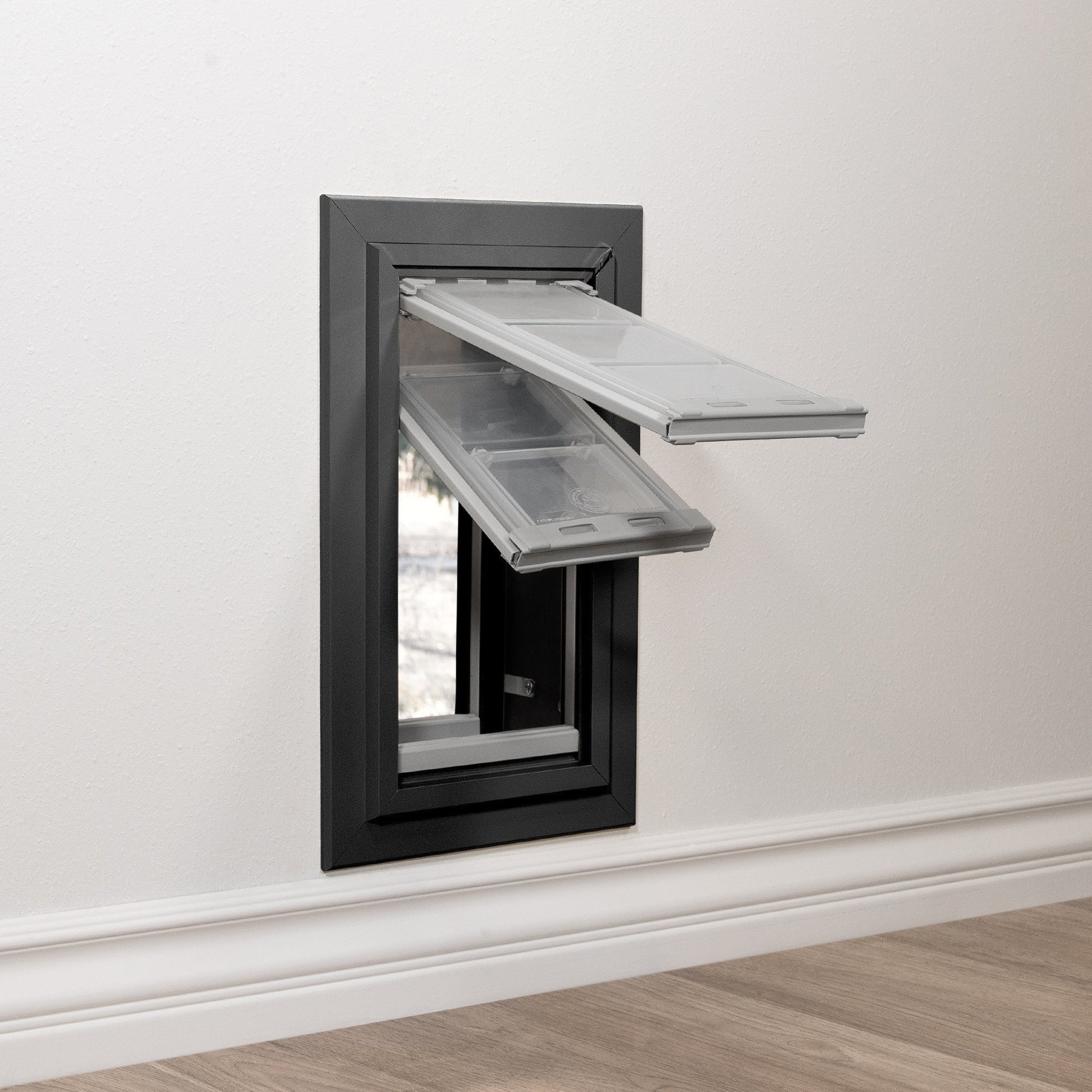 A pet door with clear flaps is installed in a white wall.