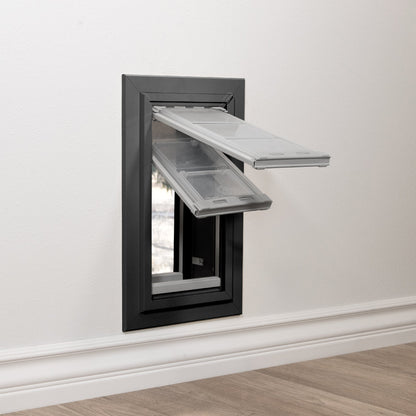 A pet door with clear flaps is installed in a white wall.
