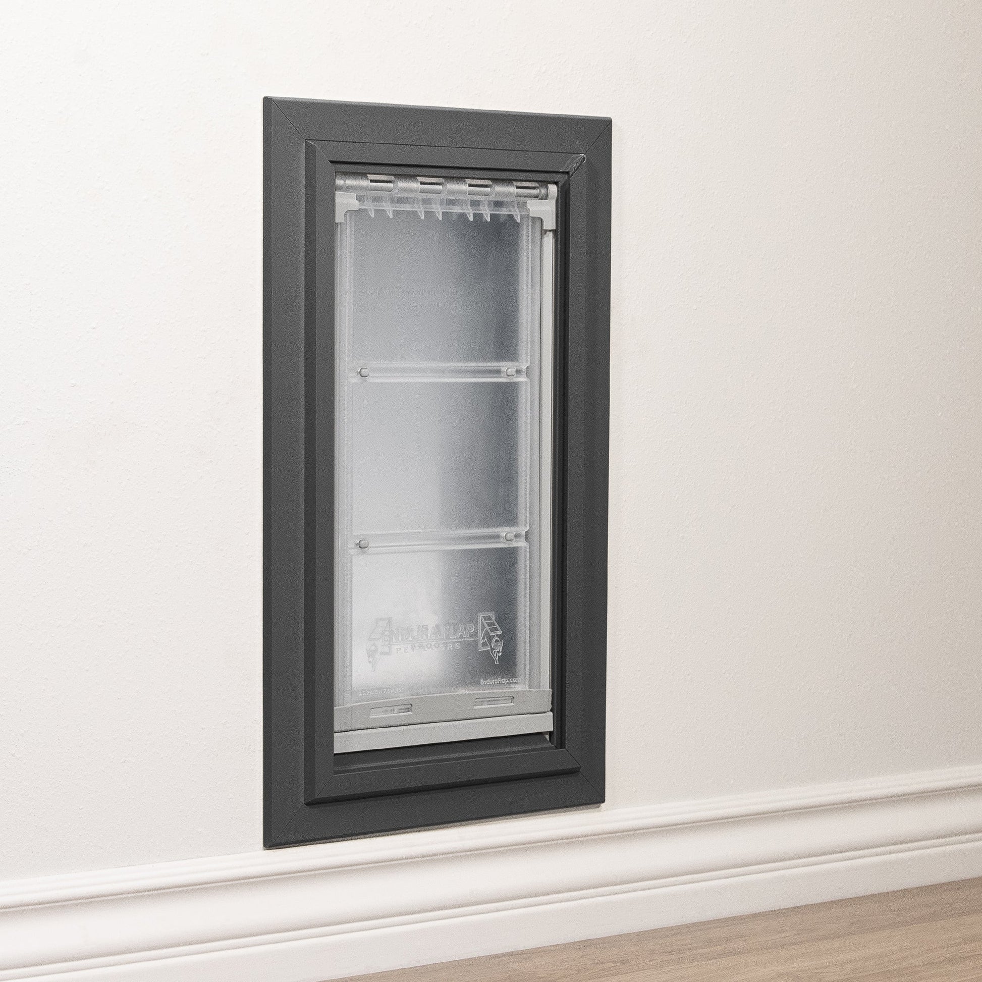 A pet door with a gray frame is installed in a white wall.