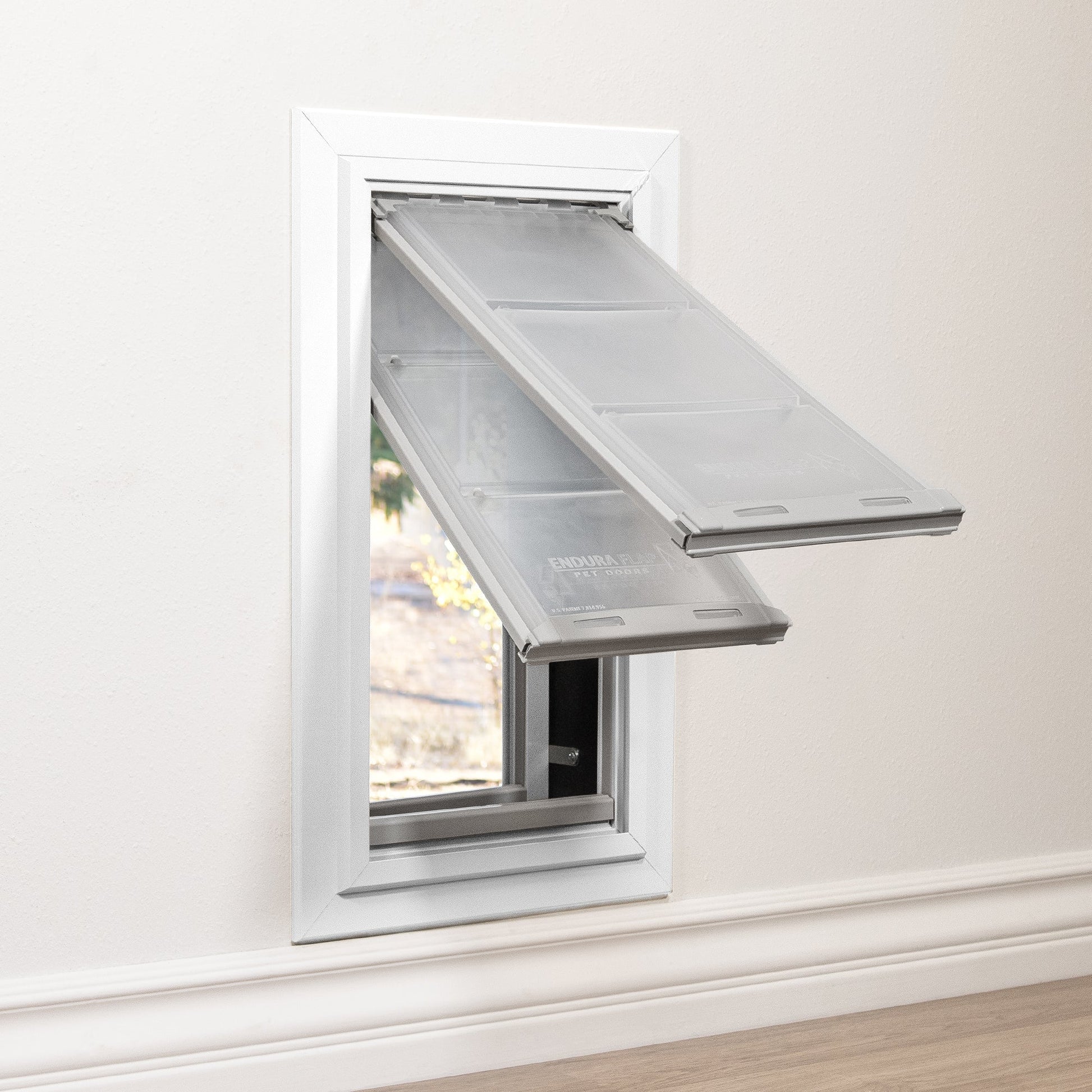 A pet door with transparent flaps is installed in a wall.