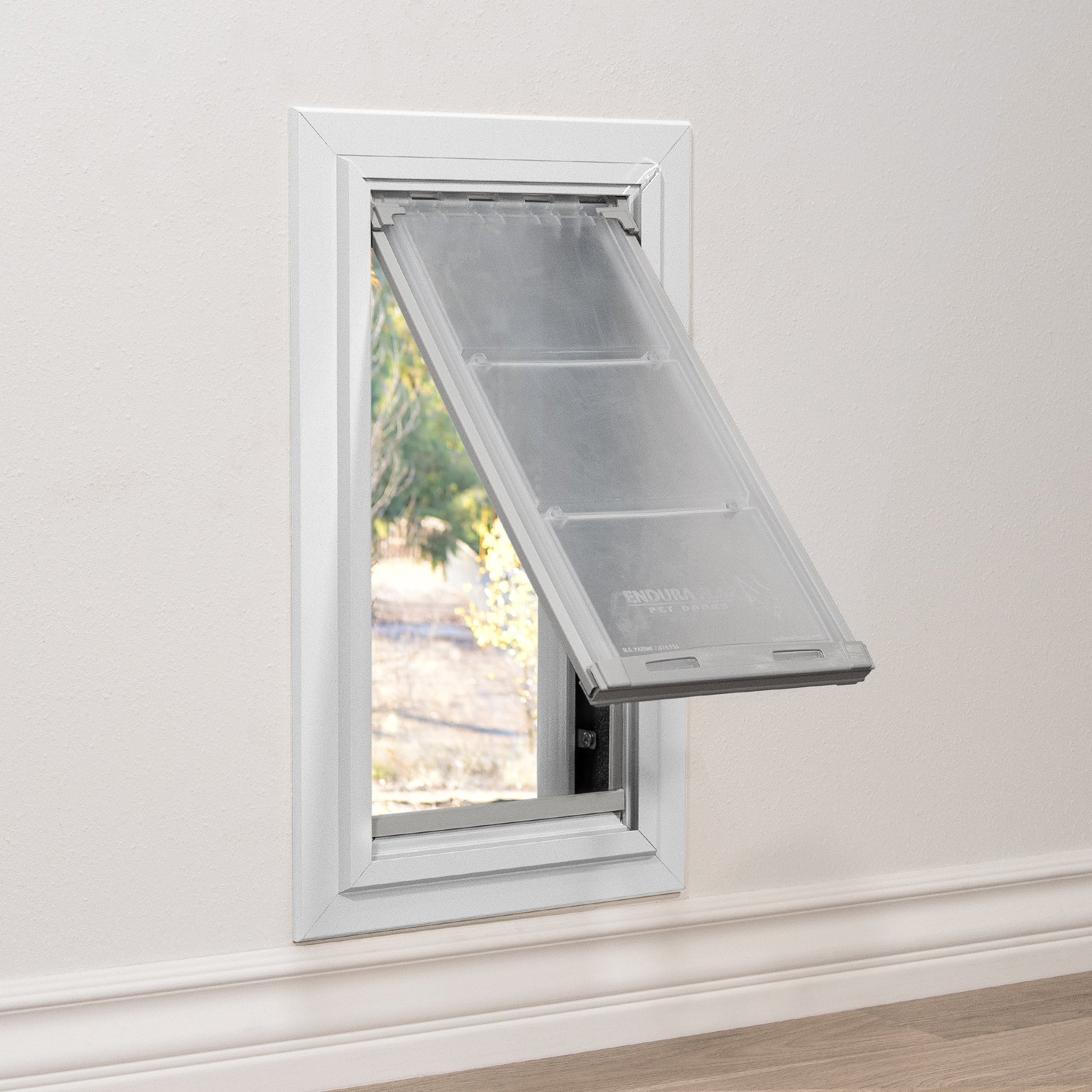 A pet door is installed in a white wall, with the clear flap partially open.