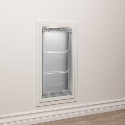 A pet door with a clear, hinged flap is installed in a white wall.