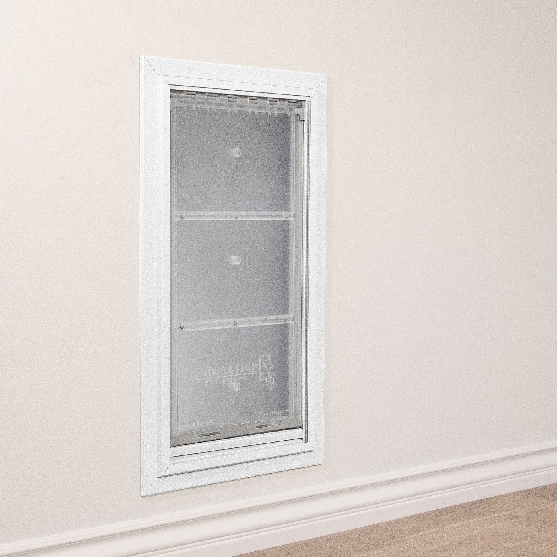 A white-framed "Endura Flap" pet door is installed in a beige wall above white trim.