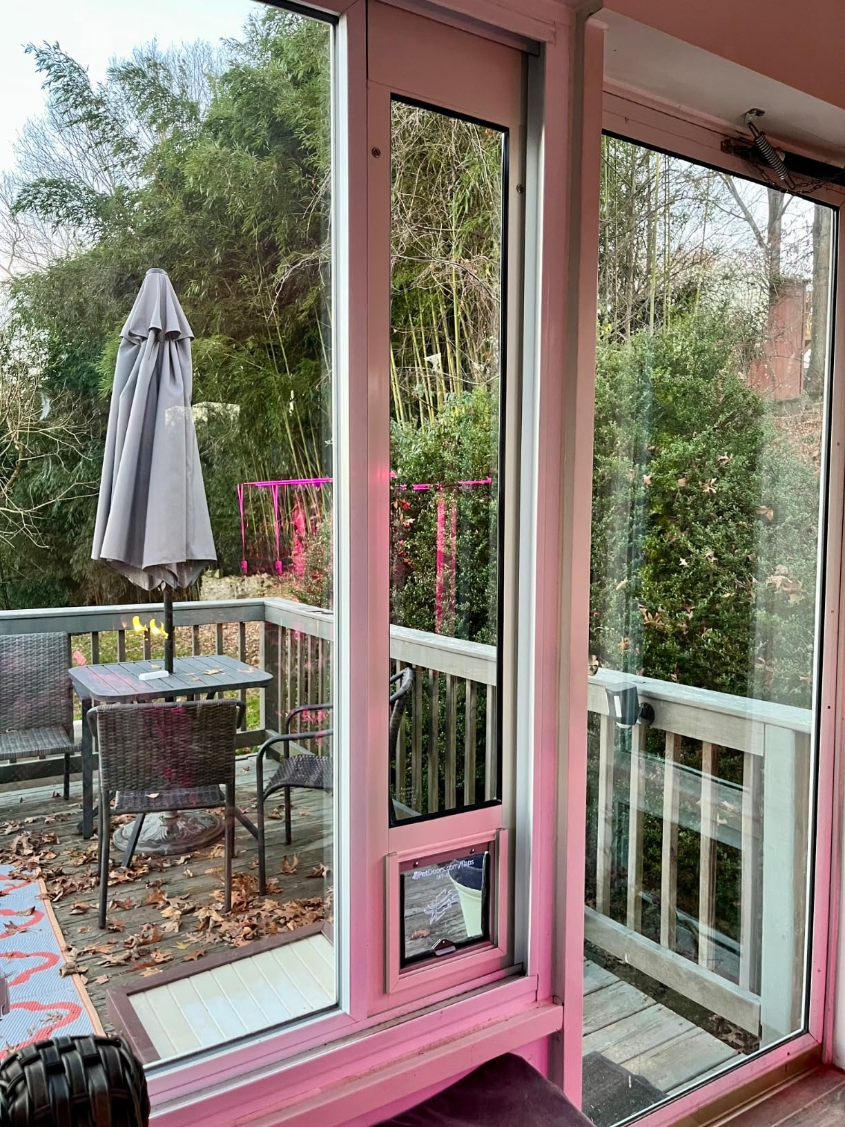 A patio with table and chairs is seen through a glass door with a pet door.