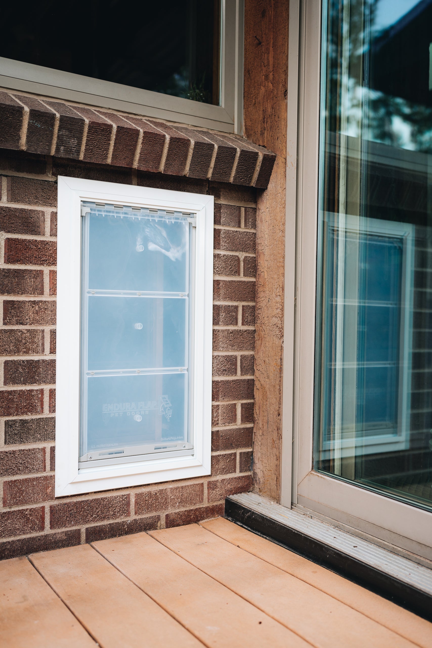 A pet door is installed in a brick wall next to a sliding glass door.